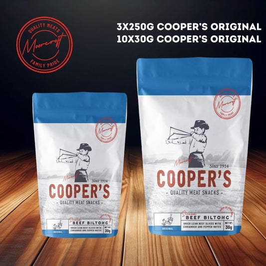 Two packets of Cooper's Original Beef Biltong are presented against a dark backdrop with the Moorcroft Family Pride seal clearly visible, suggesting a legacy of quality meat snacks. The text overlay indicates a bulk offering, with '3x250g Cooper's Original' and '10x30g Cooper's Original' packages. The bags are featured on a polished wooden surface, each detailing the classic taste of dried lean beef slices with coriander and pepper notes